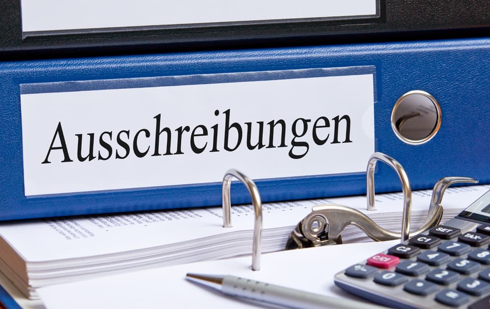 Schreibtisch mit Papieren, Taschenrechner und blauem Ordner mit Aufschrift "Ausschreibungen" | Motiv © DOC RABE Media - Fotolia.com | © Fotolia.com, Mai 2014