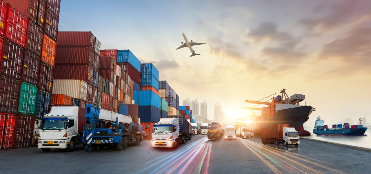 Containerfracht mit LKWs am Hafen. Am Himmel fliegt ein Flugzeug. | Motiv ©Travel mania - stock.adobe.com | © stock.adobe.com, November 2022