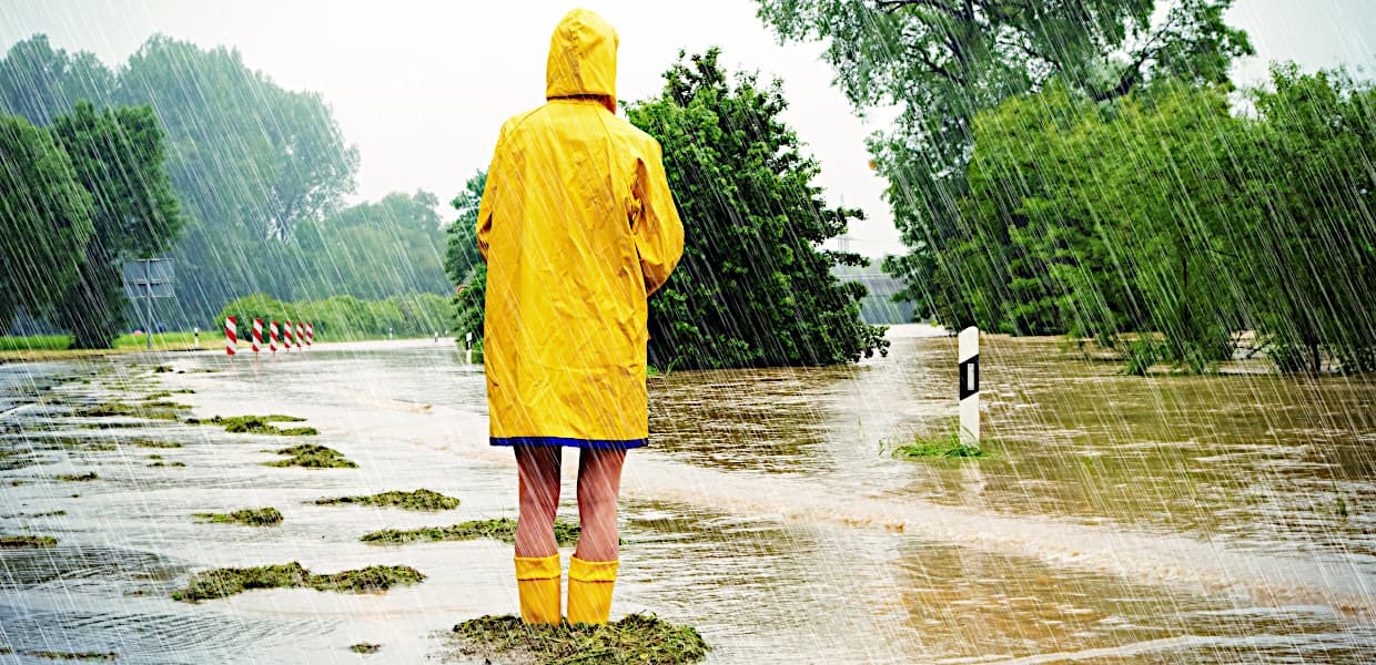 Person mit gelben Regenmantel schaut auf überschwämmte Straße | Motiv ©Jürgen Fälchle - stock.adobe.com | © stock.adobe.com, März 2021