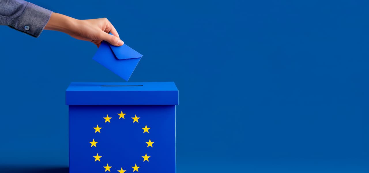 Eine Hand wirft ein blaues Kuvert in eine blaue Wahlurne mit Europasternen vor blauem Hintergrund | Motiv ©mozZz-stock.adobe.com | © stock.adobe.com, Juni 2024