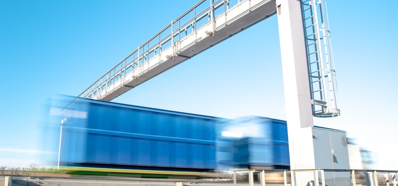 A Maut 1 Heauder (jpg) | Motiv ©edojob-stock.adobe.com | © stock.adobe.com, Januar 2017 Blauer LKW fährt über die Autobahn durch die Mautstelle. Im Bild ist eine Bewegungsunschärfe zu erkennen. | Motiv ©edojob-stock.adobe.com | © stock.adobe.com, Januar 2017